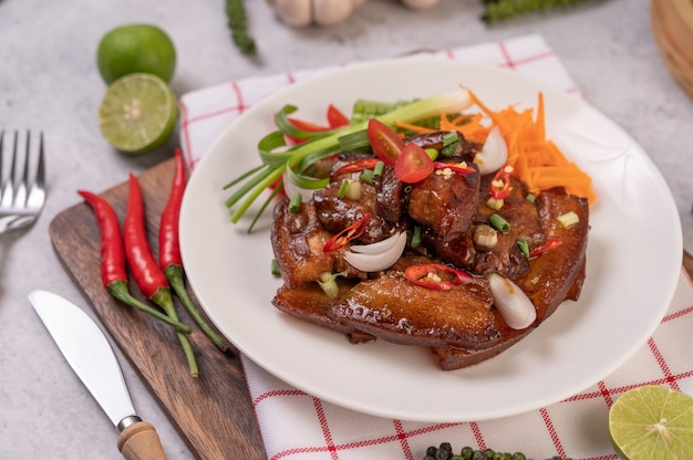 Dulce de cerdo en un plato blanco con cebolletas picadas, ají, lima, calabaza, tomate y ajo.