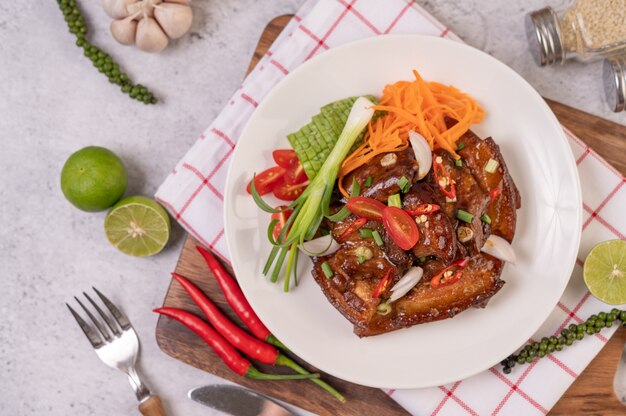 Dulce de cerdo en un plato blanco con cebolletas picadas, ají, lima, calabaza, tomate y ajo.