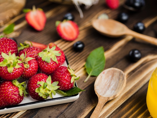 Dulce fresas frescas y cucharas sobre fondo de madera