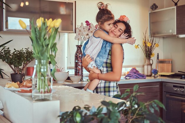 La dulce niña besa a su madre mientras se sienta en sus brazos en la cocina.