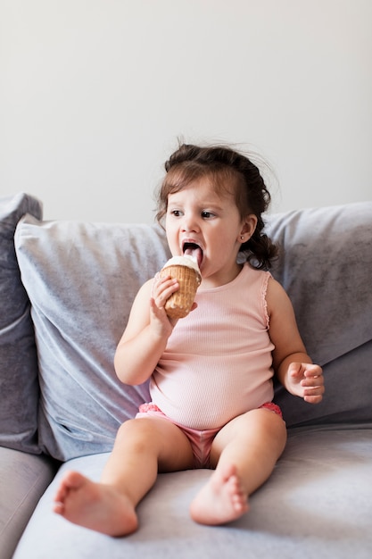 Dulce niña comiendo un helado en el sofá