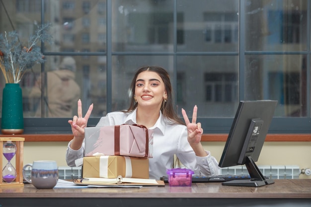 Dulce niña sentada en el escritorio y signo de paz con las manos