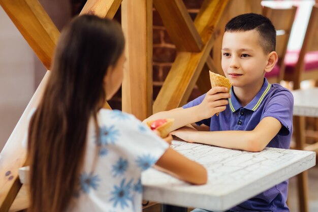 Dulce niño comiendo helado sentado en una silla alta en el restaurante