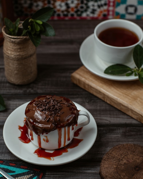 Una dulce taza de mousse de chocolate sabroso con jarabe de fresa en el interior servido con una taza de té