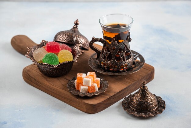 Dulces caramelos de colores y té fragante en tablero de madera