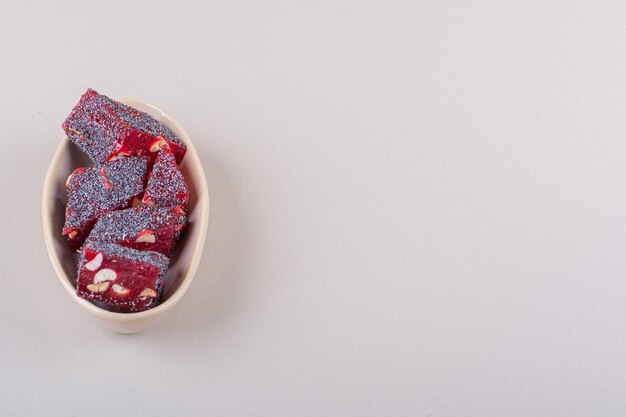 Dulces caramelos rojos con nueces en un tazón de color beige sobre fondo blanco. Foto de alta calidad