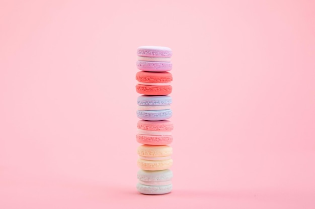 Dulces y coloridos macarons franceses apilados uno encima del otro sobre fondo rosa