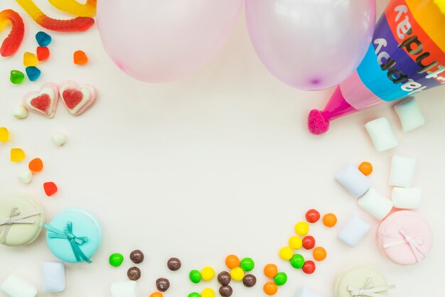 Dulces; malvavisco; globos y sombrero de cumpleaños en fondo blanco