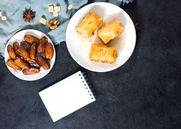 Dulces orientales con dátiles frutales y bloc de notas.