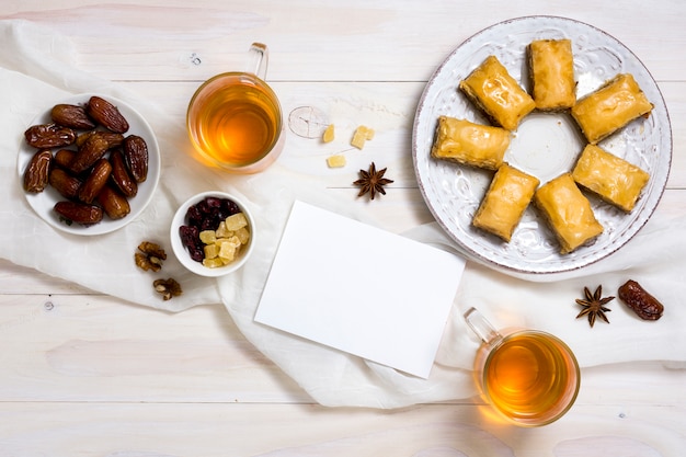 Dulces orientales con dátiles frutales y papel en blanco.