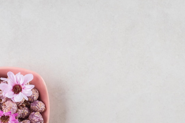 Foto gratuita dulces de palomitas de maíz marrón y flores en un tazón de color rosa sobre la mesa de mármol.