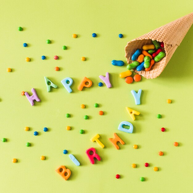 Dulces que se derraman desde el cono de helado de galleta en feliz cumpleaños sobre la superficie verde