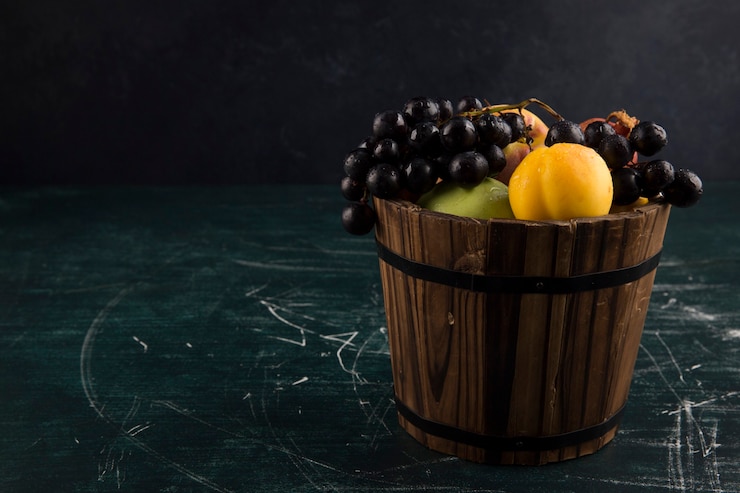Foto gratuito duraznos y uvas en un balde de madera en pizarra