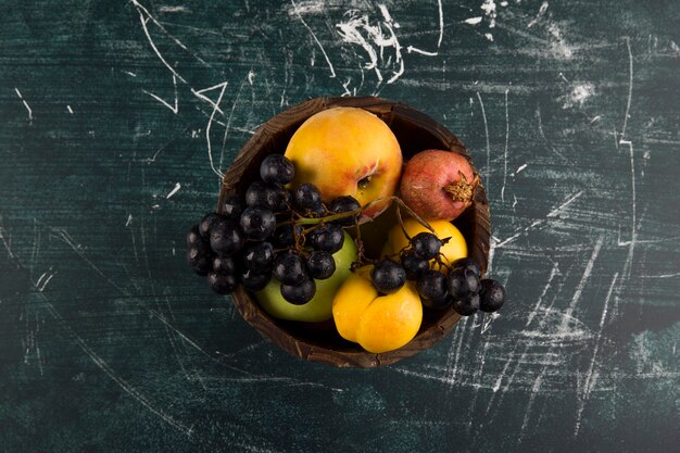 Duraznos y uvas en un cuenco de madera sobre pizarra en el centro