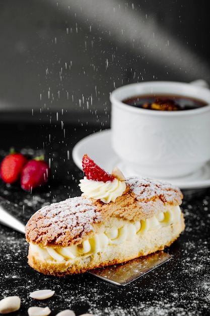 Eclair con crema de fresa y una taza de té sobre la mesa