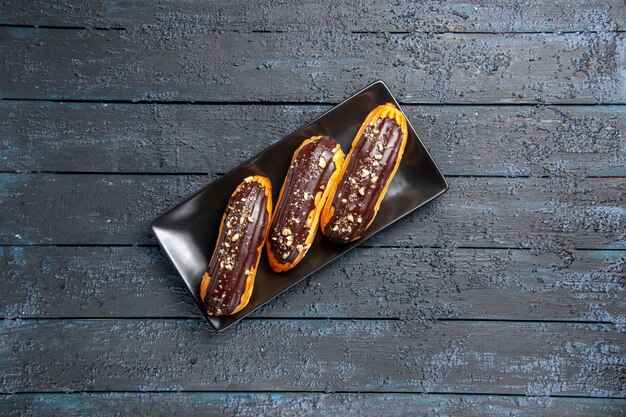 Eclairs de chocolate de vista distante superior en placa rectangular oscura sobre fondo de madera oscura