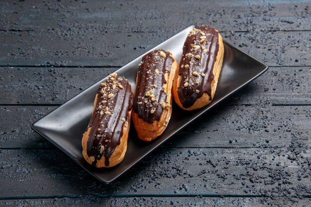 Eclairs de chocolate de vista inferior en placa rectangular sobre la mesa de madera oscura con espacio libre