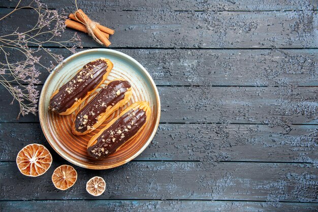 Eclairs de chocolate de vista superior en placa ovalada rama de flor seca y limones secos en el lado izquierdo de la mesa de madera oscura con espacio de copia