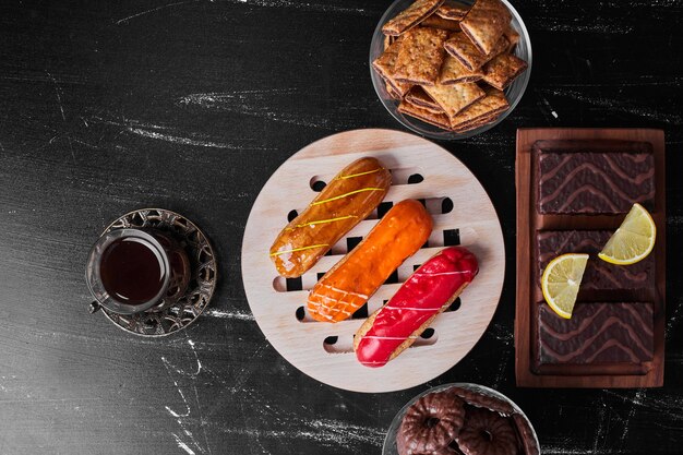 Eclairs con salsas de frutas encima servidos con té y brownies.