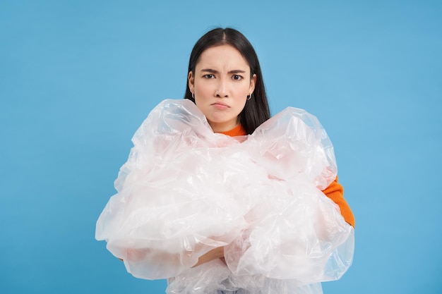 Ecología y reciclaje joven ecoactivista enojada sostiene bolsas de plástico con la cara molesta recogiendo