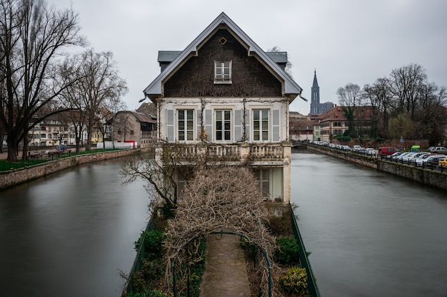 Edificio antiguo rodeado de agua y vegetación bajo un cielo nublado en Estrasburgo en Francia