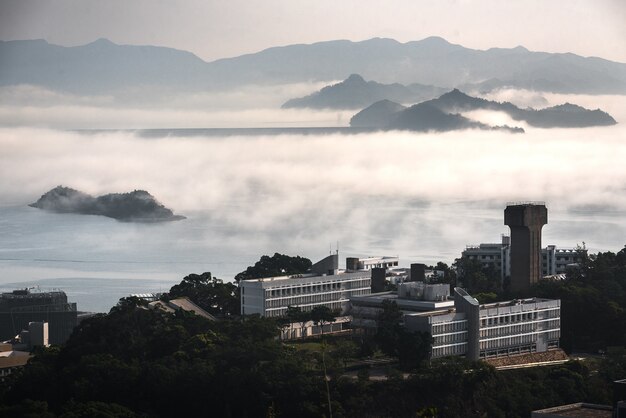 Edificios rodeados de árboles, agua y montañas cubiertas de niebla