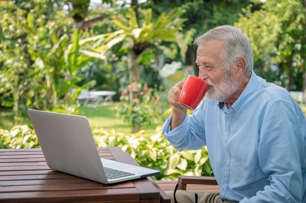 Ejecutivo senior con cabello blanco usando computadora portátil trabajando en casa tomando café mirando la cámara