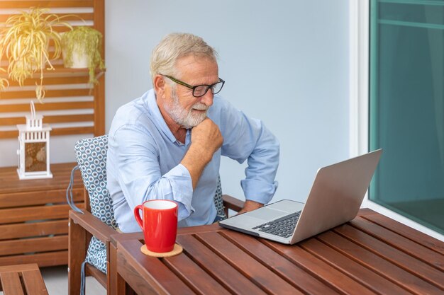 Ejecutivo senior de cabello blanco usando computadora portátil viendo películas en casa con café