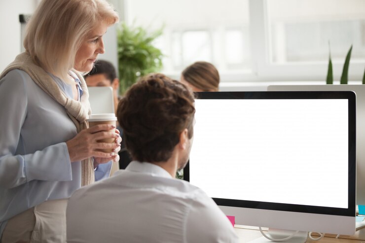 Foto gratuito ejecutivo senior revisando informe anual en pantalla de computadora ayudando a colega