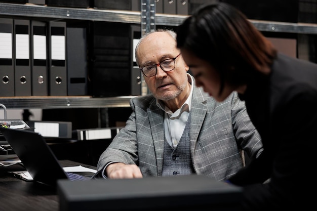 Foto gratuita ejecutivos profesionales de contabilidad que imputan papeleo de datos administrativos de contabilidad en una computadora portátil. sala de archivo de la burocracia llena de carpetas y diagramas