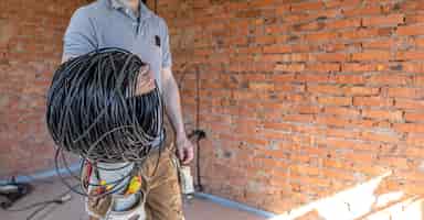 Foto gratuita un electricista con un casco mira la pared mientras sostiene un cable eléctrico