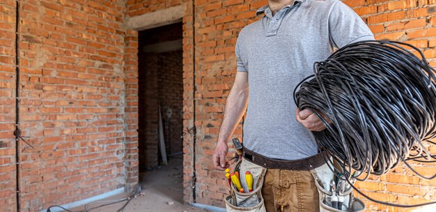 Un electricista con un casco mira la pared mientras sostiene un cable eléctrico