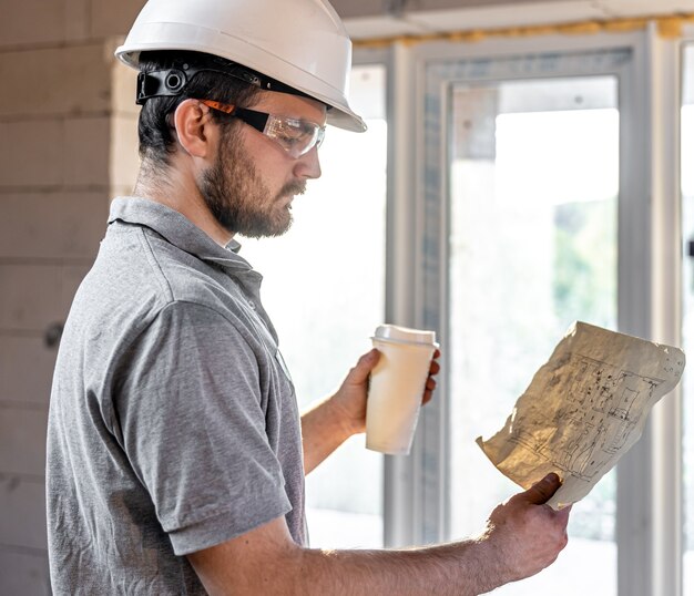 Un electricista está estudiando un dibujo de construcción con un café en la mano.