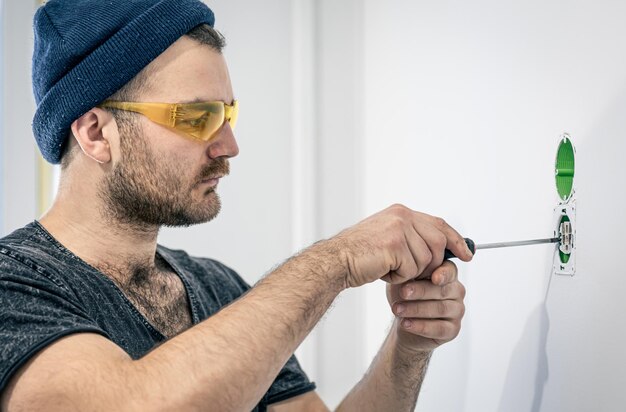 Un electricista está montando enchufes eléctricos en la pared blanca en el interior