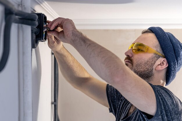 Un electricista está montando enchufes eléctricos en la pared blanca en el interior