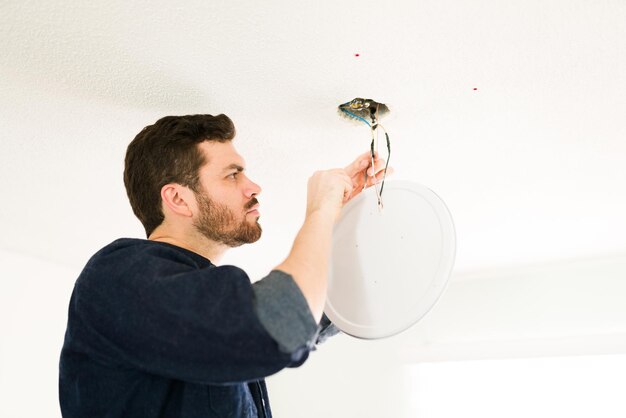 Electricista hispano profesional arreglando el sistema eléctrico en el techo y cortando algunos cables en casa