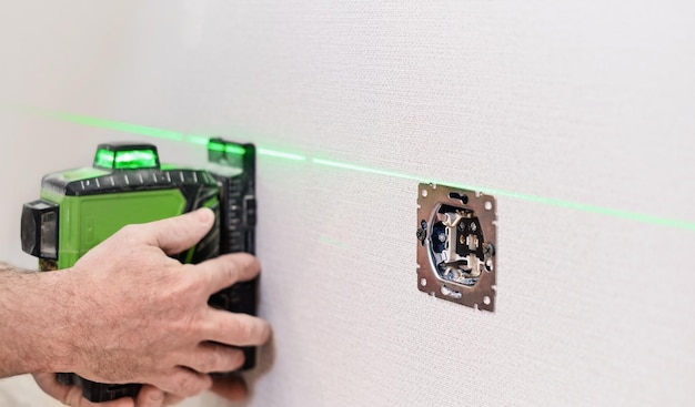 Un electricista instala enchufes en el apartamento Comprobación de los enchufes instalados en la pared del apartamento con un enfoque selectivo de nivel láser en los enchufes