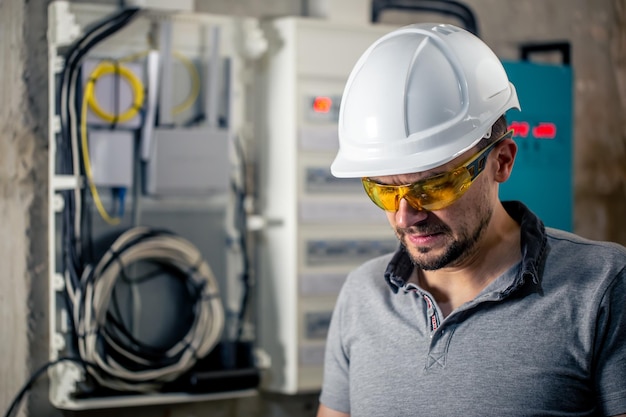 Electricista masculino con gafas de seguridad y casco cerca de la centralita