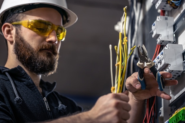 Un electricista masculino trabaja en una centralita con un cable de conexión eléctrica