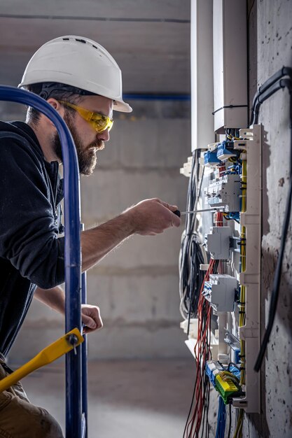 Un electricista masculino trabaja en una centralita con un cable de conexión eléctrica