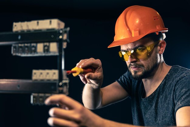 Un electricista masculino trabaja en un cuadro de distribución con un cable de conexión eléctrica