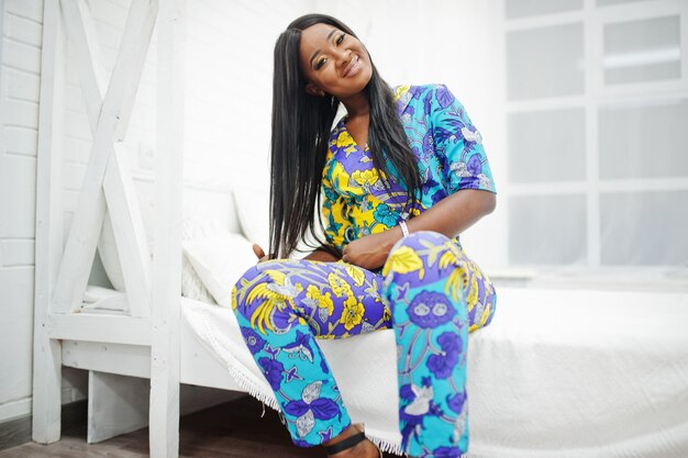 Elegancia mujer afroamericana modelo usar ropa de colores Chic mujeres afro en la habitación sentada en la cama