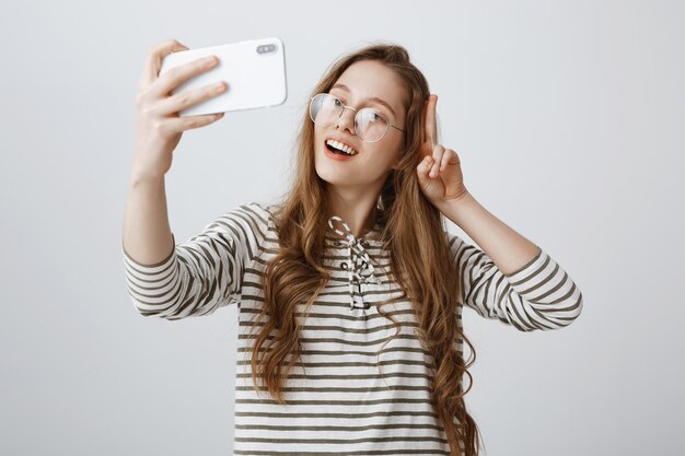 Elegante adolescente tomando selfie en smartphone, sonriendo feliz