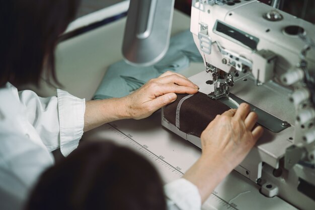 Elegante anciana sentada en estudio y coser tela