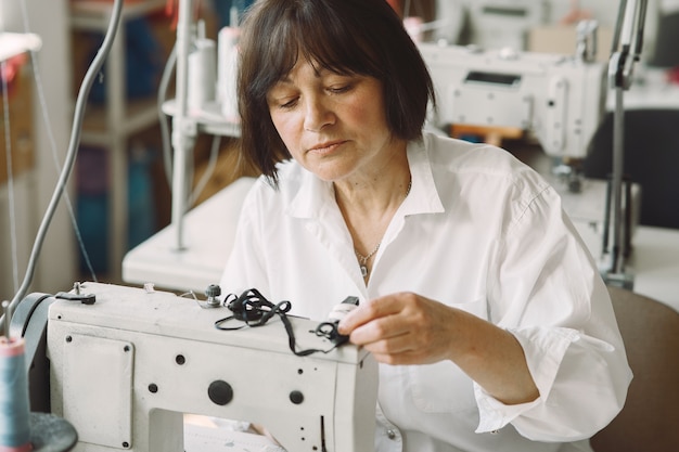 Elegante anciana sentada en estudio y coser tela