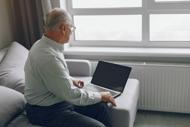 Elegante anciano sentado en casa y usando una computadora portátil