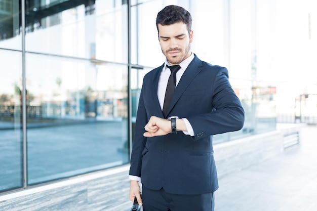 Elegante y apuesto hombre de negocios latino revisando la hora en su reloj en la ciudad