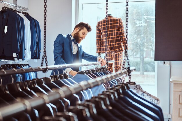 Elegante asistente de tienda barbudo vestido con un elegante traje azul que trabaja en una tienda de ropa masculina.