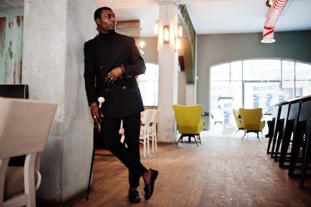 Elegante caballero afroamericano con elegante chaqueta negra que sostiene un bastón retro como matraz de caña o bastón bastón con mango de bola de diamante dorado Hombre afro rico de moda