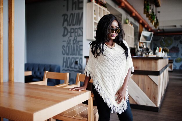 Elegante chica afroamericana con gafas de sol posadas en un café moderno